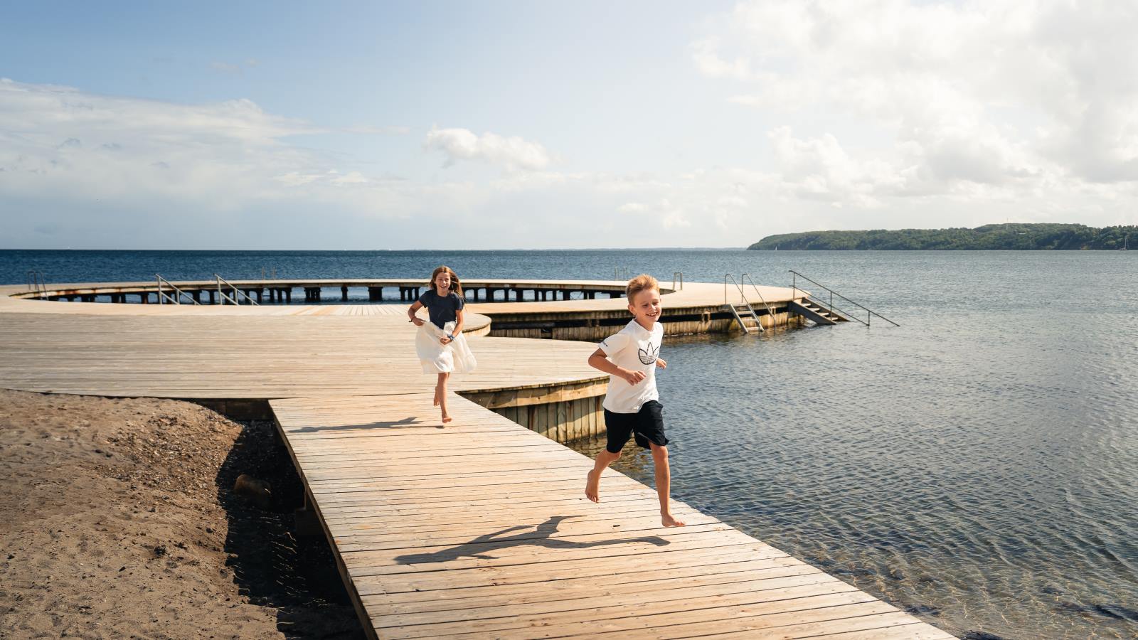 Pige og dreng løber på cirkelbroen på Østerstrand i sommervejr