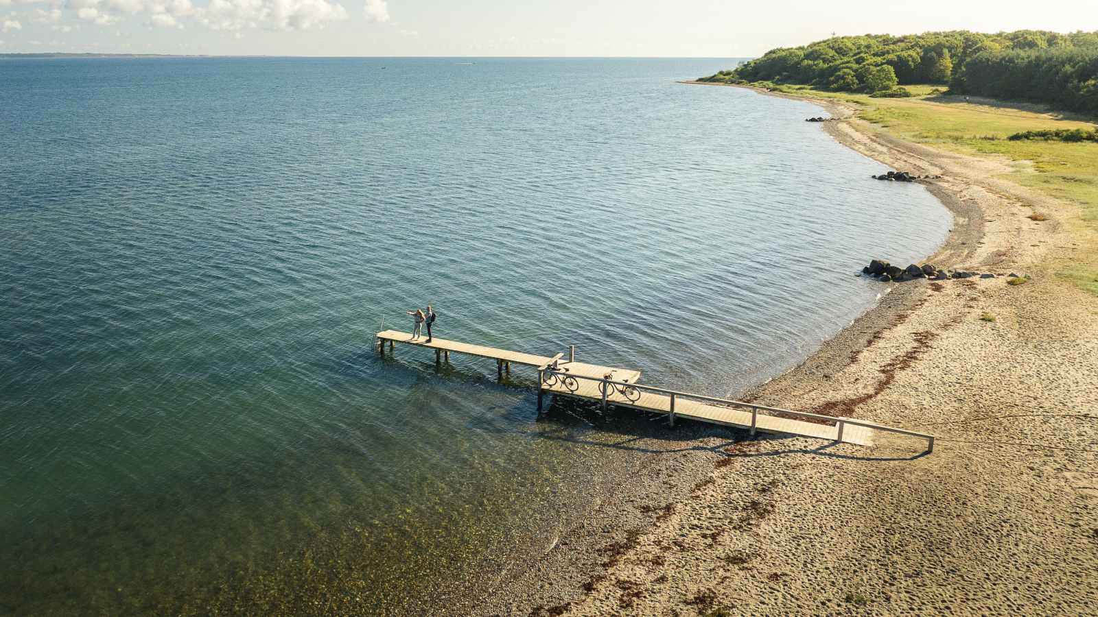 Cykelturister står og kigger ud over vandet på stranden ved Trelde Næs
